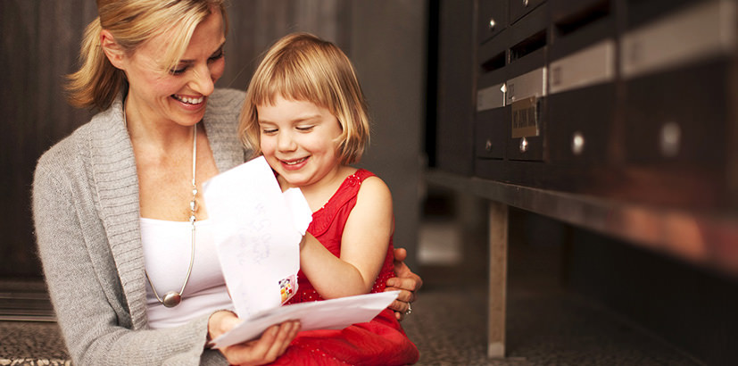 Woman with little girl sitting in front of mailboxes opening letters