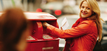 Happy woman posting mail in the red post box