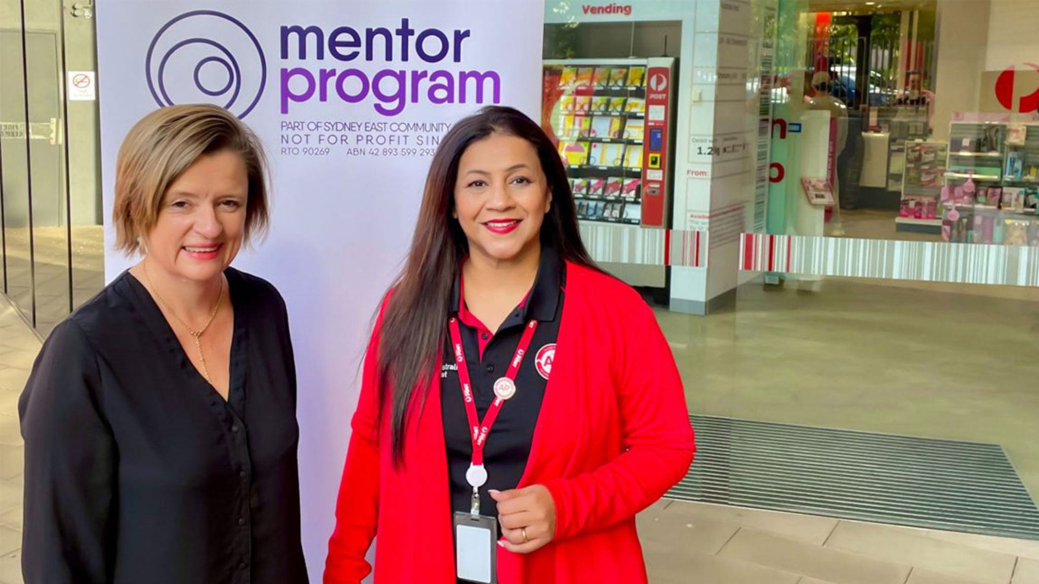 Two women stand in front of a banner reading 'mentor program'