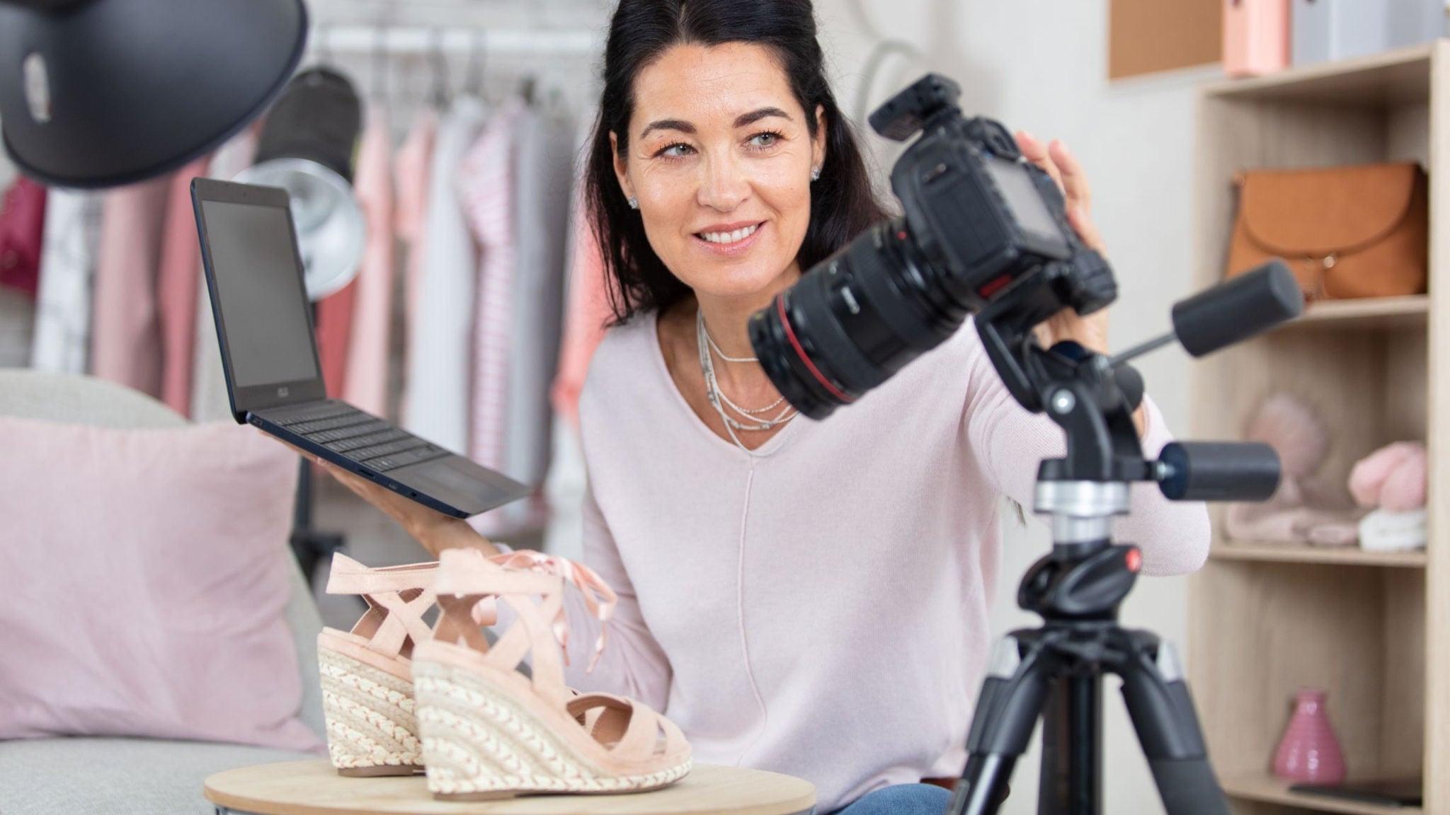 A woman records a video of pink wedge sandals using a digital camera on a tripod