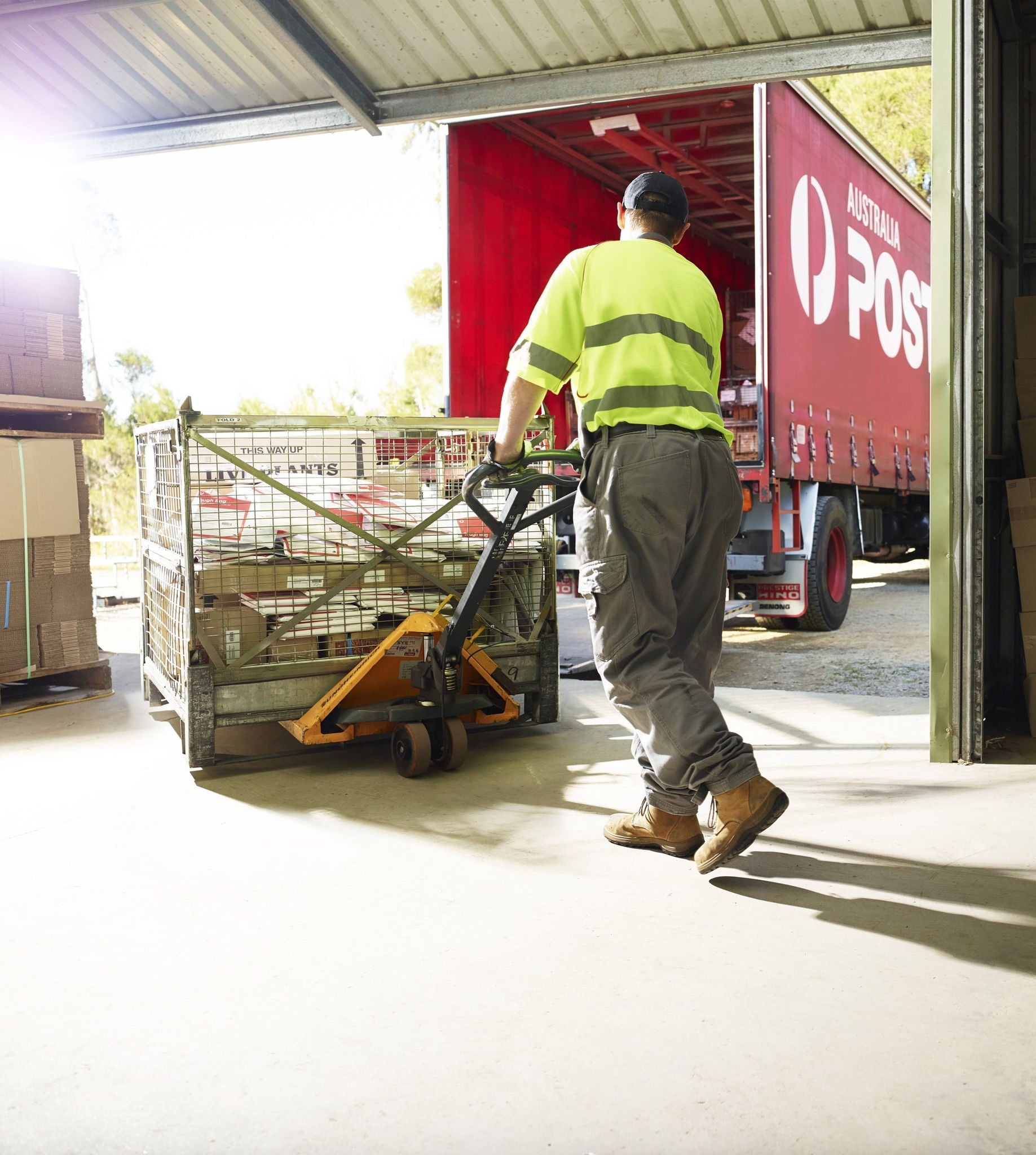 man in Australia Post uniform pushing a ULD using a pallet jack towards the rear of an Australia Post truck