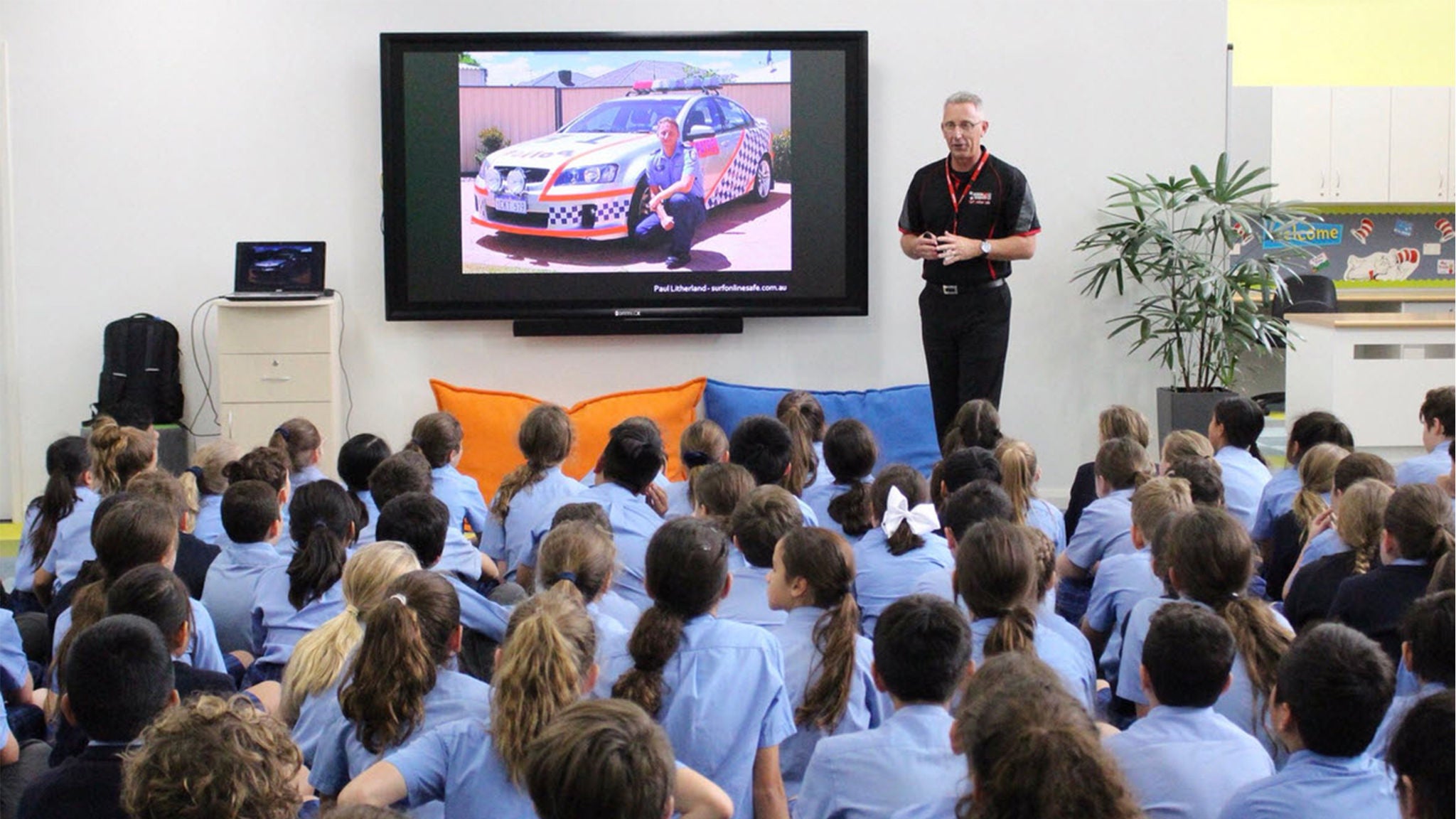A man delivering a presentation in front of a large group of students at a school 