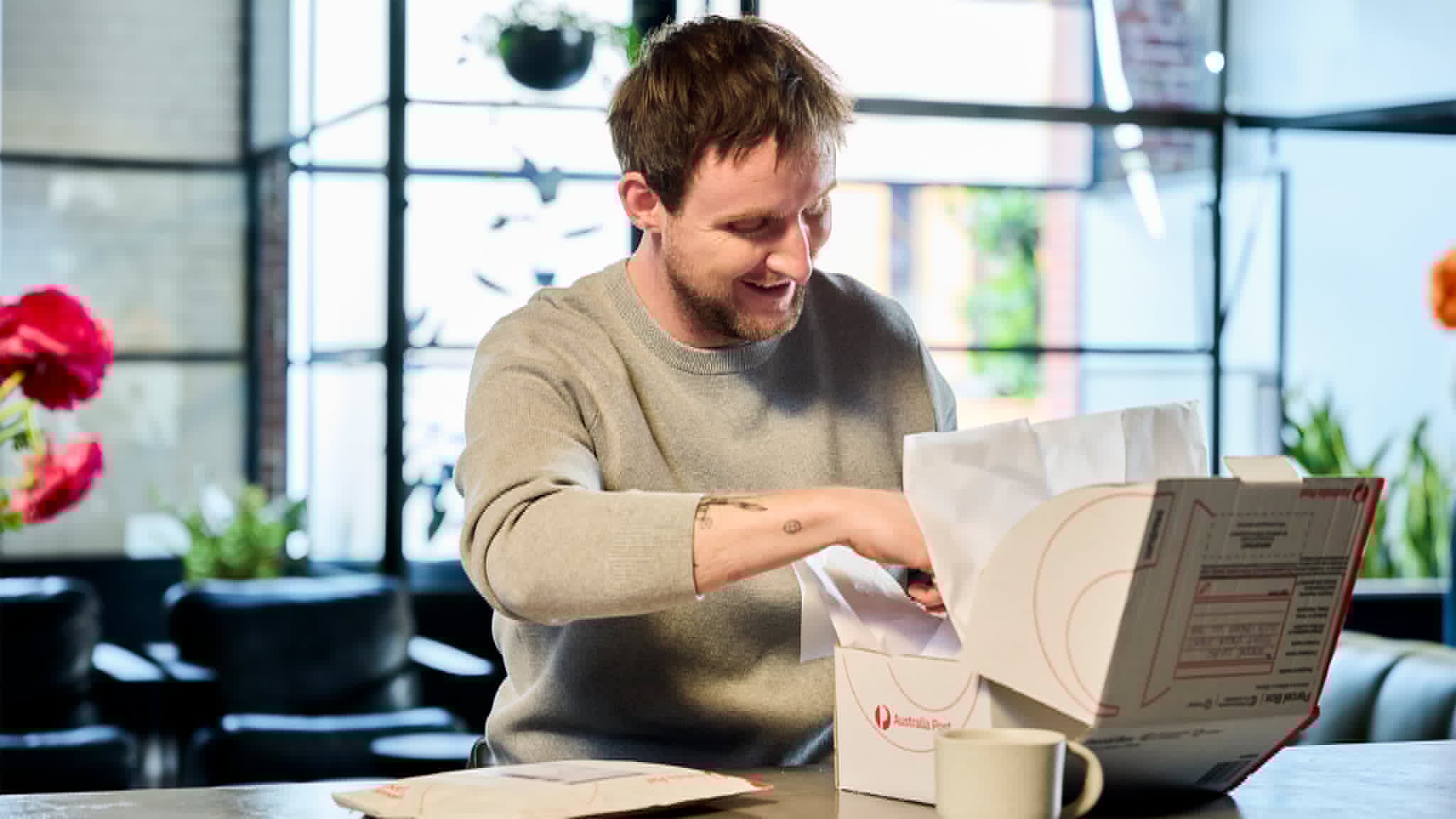 A man sits at a table opening a white shipping box
