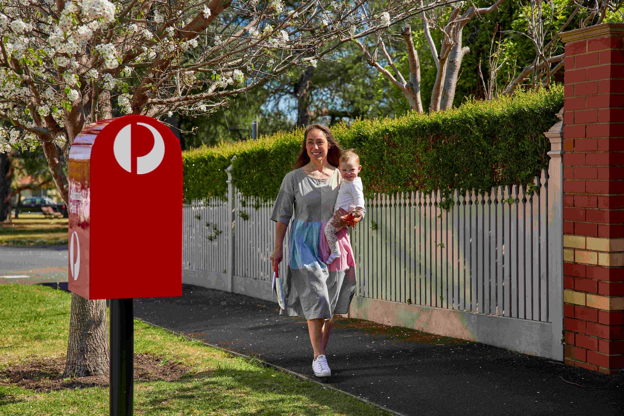A woman is walking on a suburban sidewalk carrying a young child