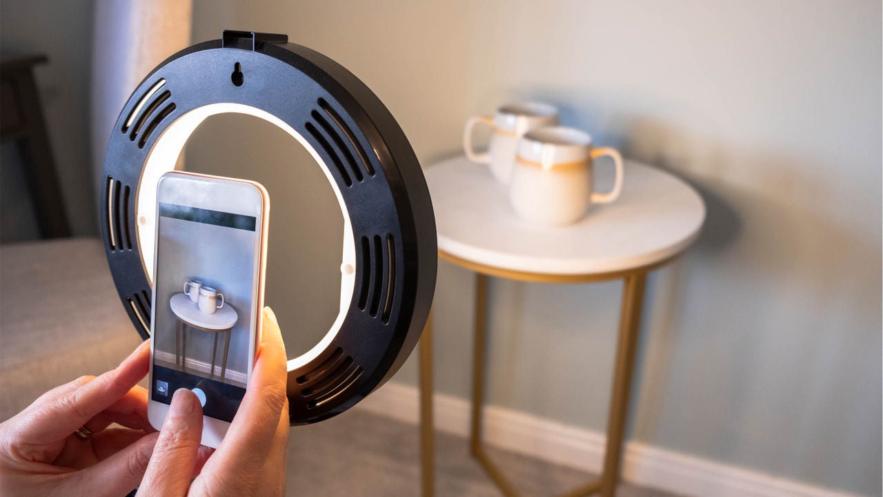 Person photographing mugs with smartphone and ring light