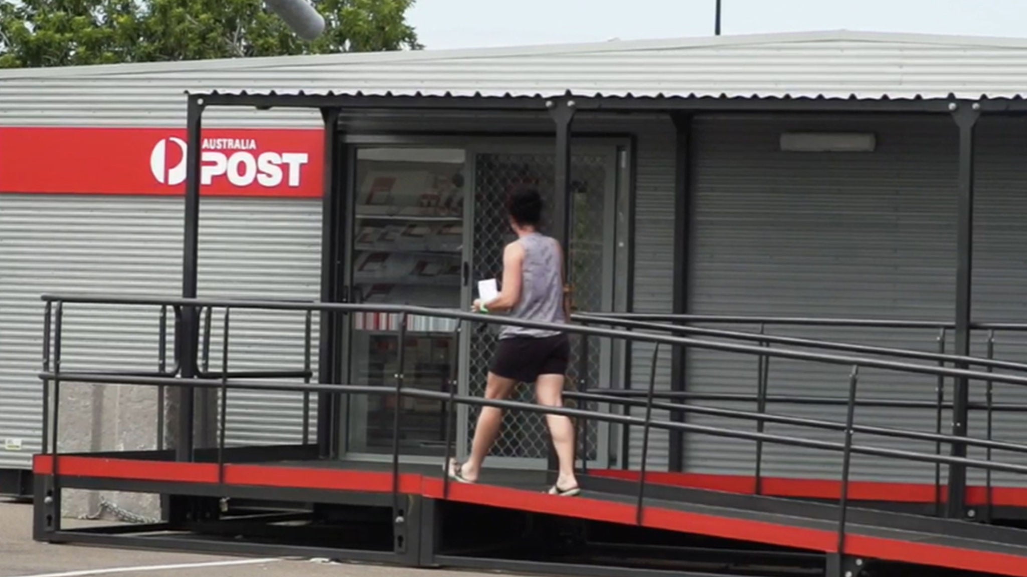 A person is walking up a ramp towards the entrance of an Australia Post office. 