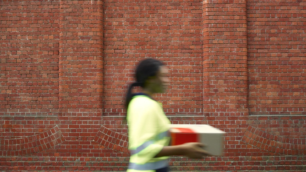 Female postie on the move, Female, Australia Post, city, letters, red, delivery, our people, postie, blue, working, Safety, Yellow, CBD, parcels, Mail, walking, Uniform, building, cream, collection, On The Move, Metro, Daytime, silver, fluorescent, polo, staff member, bricks, holding box