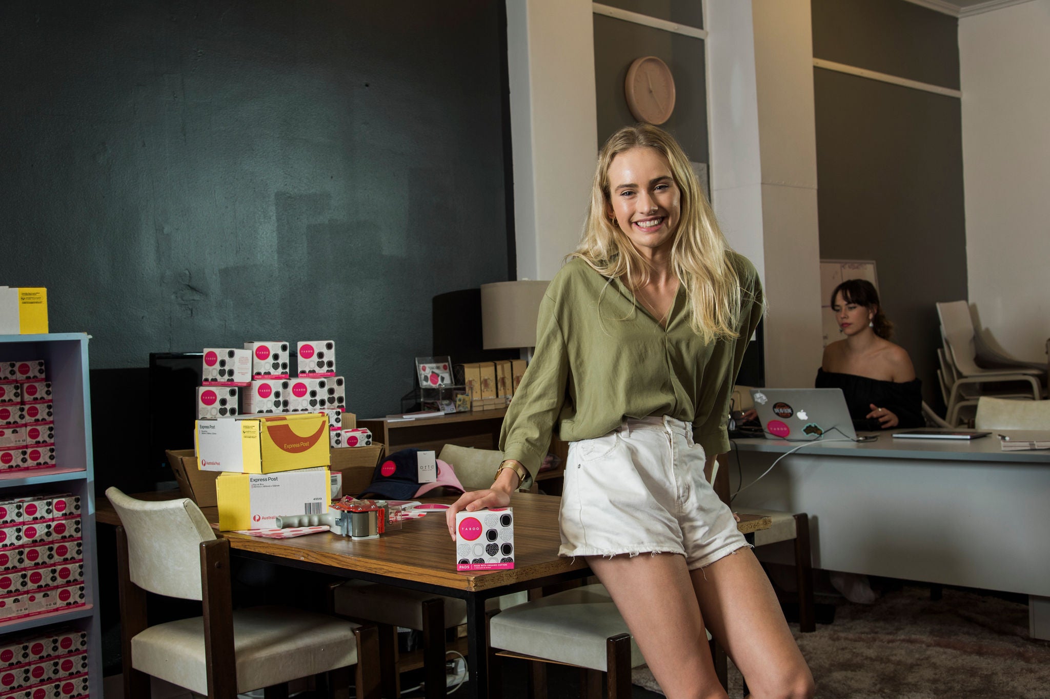 photo-taboo-woman-blonde-hair-green-shirt-sitting-on-table-packaging-boxes
