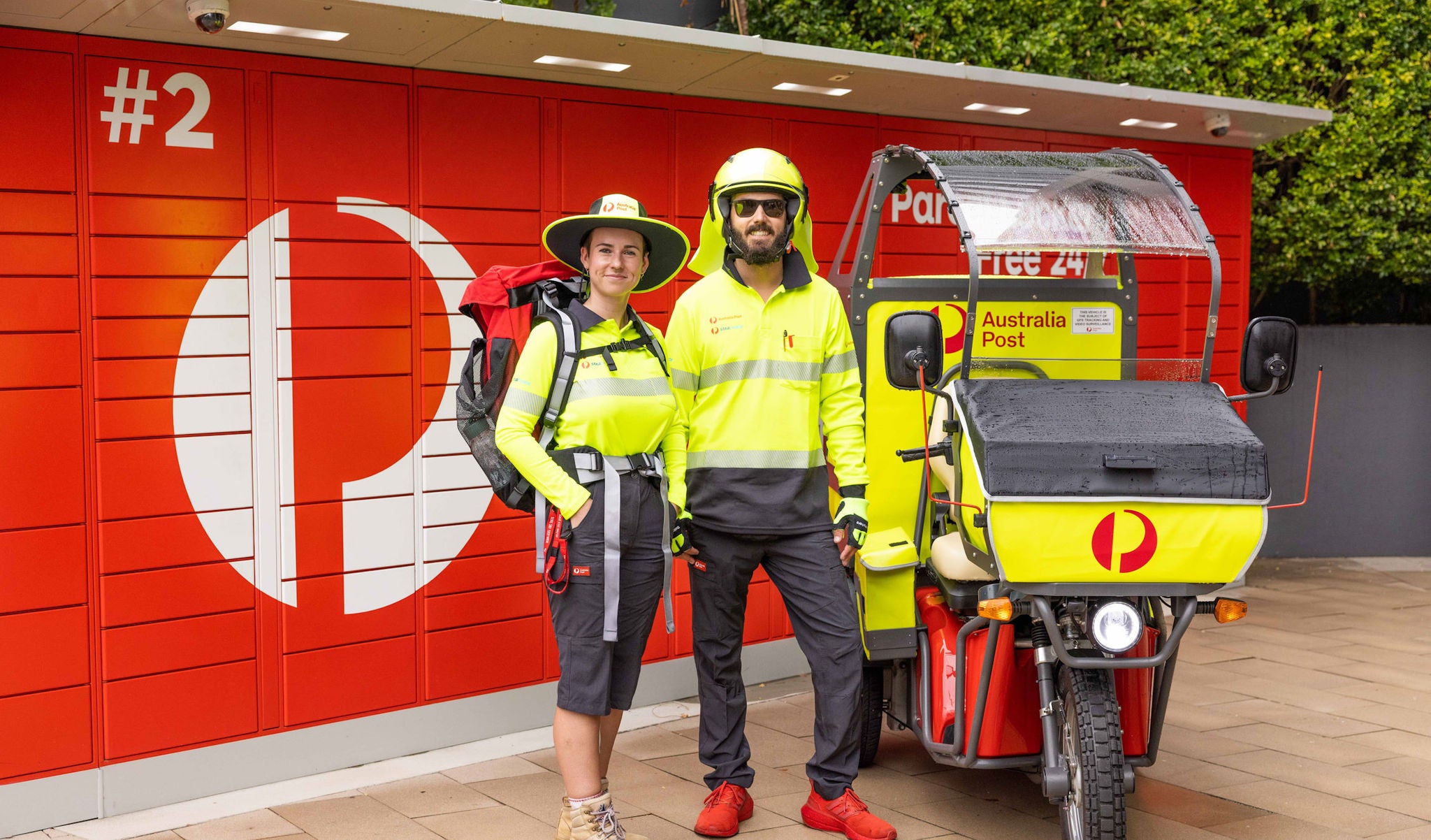 Two posties standing in front of a parcel locker