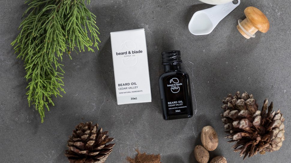 A box and bottle of beard oil surrounded by acorns and a fir tree branch