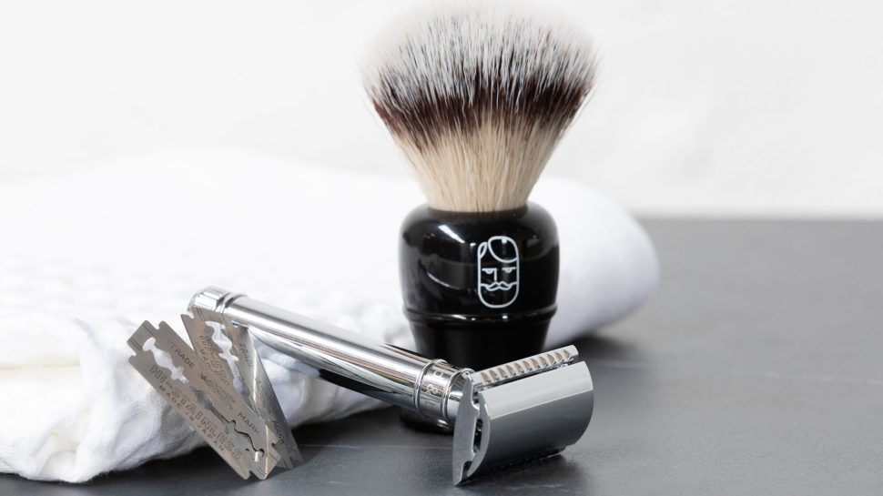 A razor, blades and shaving brush resting on a white towel