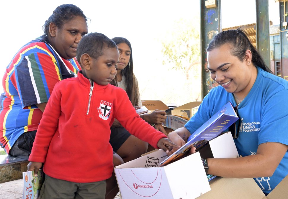 Female representative from the Indigenous Literacy Foundation shows a young Indigenous boy a picture book. 