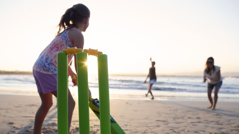 A young girl gets ready to bat during a game of beach cricket with her family.
