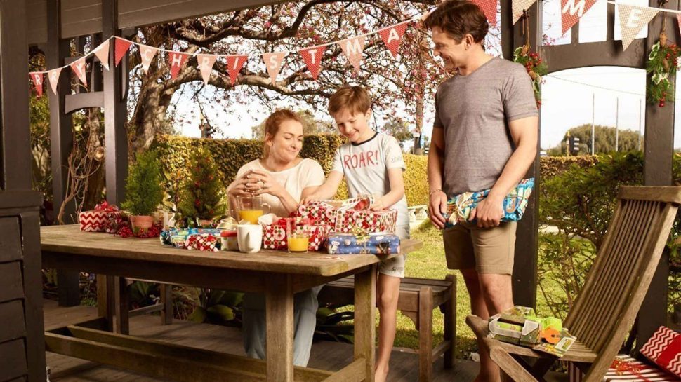 A family celebrates Christmas in the backyard as the parents watch their son open a present.