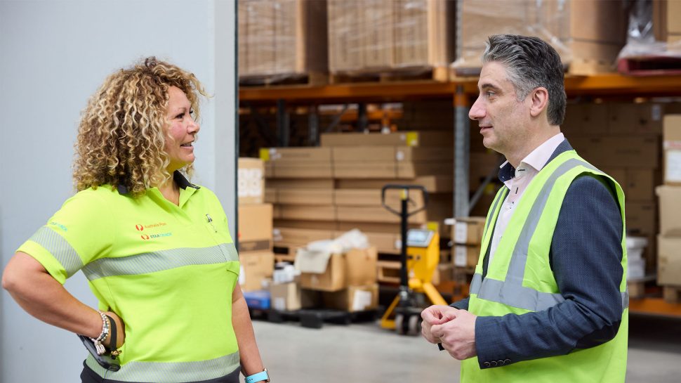 Female StarTrack driver in conversation with man in high-vis vest in a warehouse