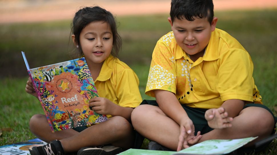 Young boy and girl sit and read an Indigenous book as part of NAIDOC week activities.
