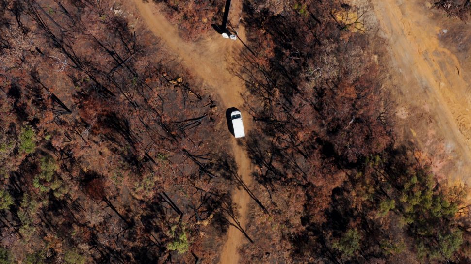 Aerial image of a white truck passing through a blackened forest.