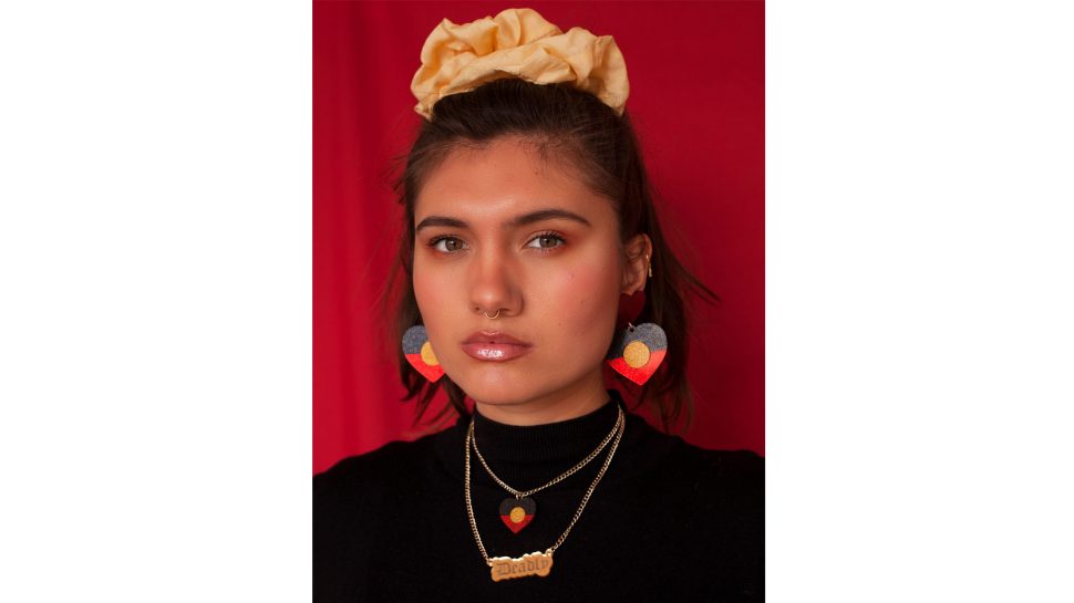 A woman wearing earrings and a necklace in the colours of the Aboriginal flag. 