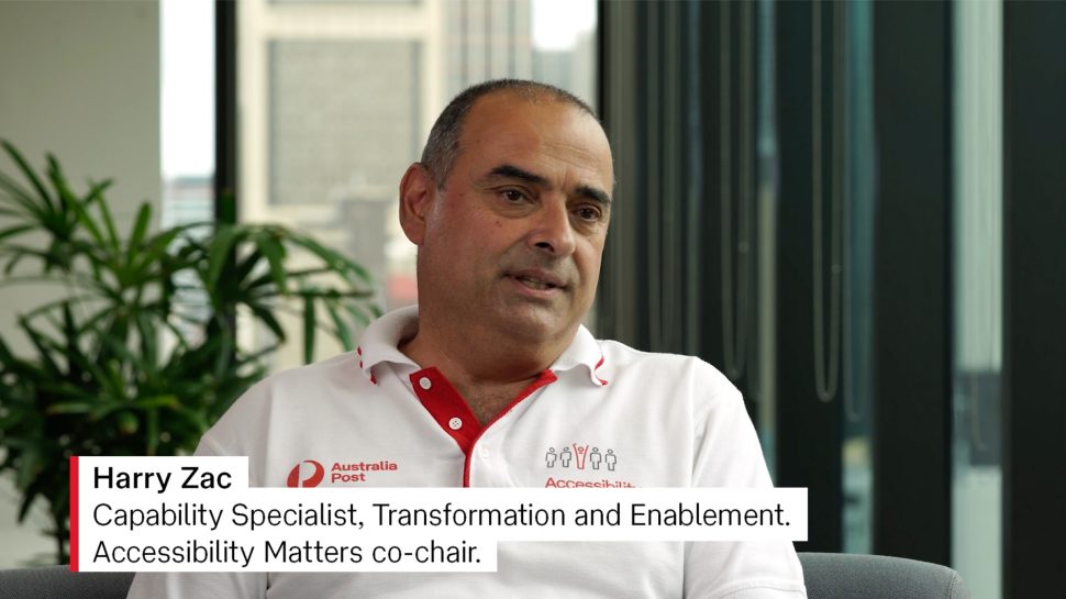 A man wearing a red and white Australia Post collared T-shirt. The words on the image read “Harry Zac Capability Specialist, Transformation & Enablement, Accessibility Matters co-chair”