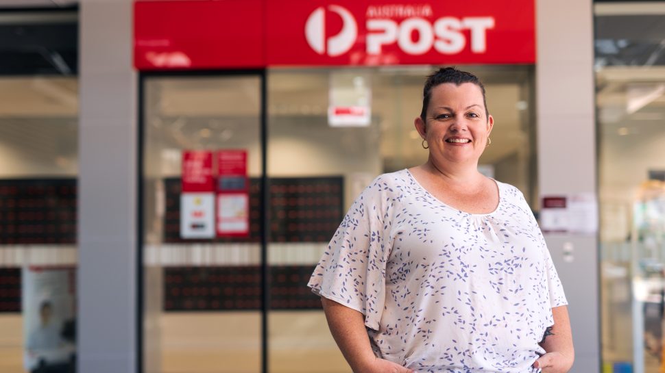 Smiling woman in white and blue blouse standing outside a Post Office
