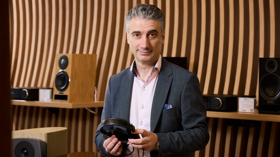 Man in a suit holding a pair of headphones with audio equipment behind him