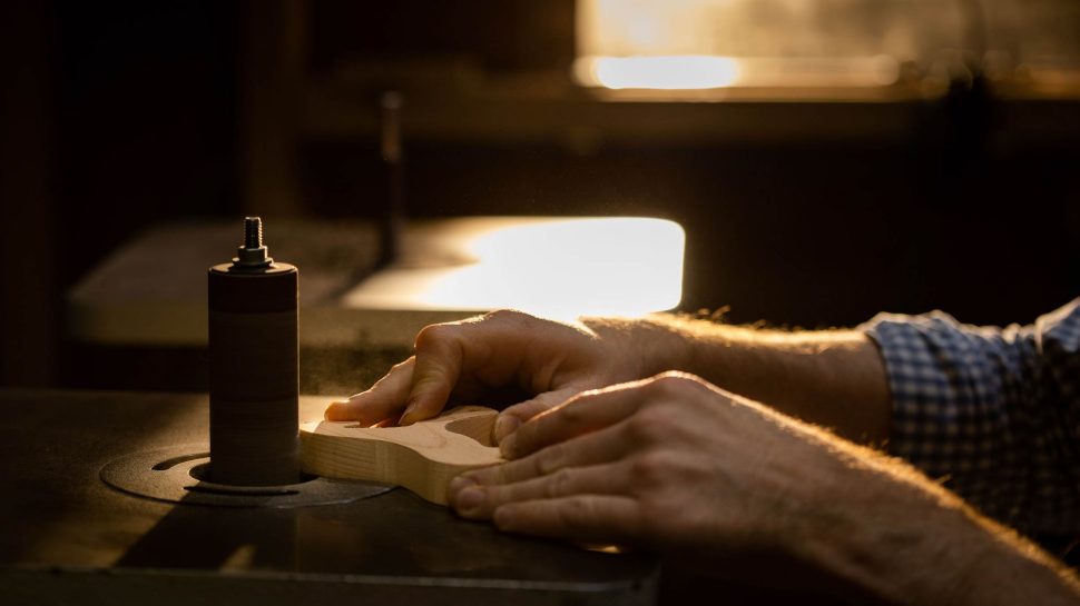 Close-up of a man’s hands using a machine to build a wooden toy. 