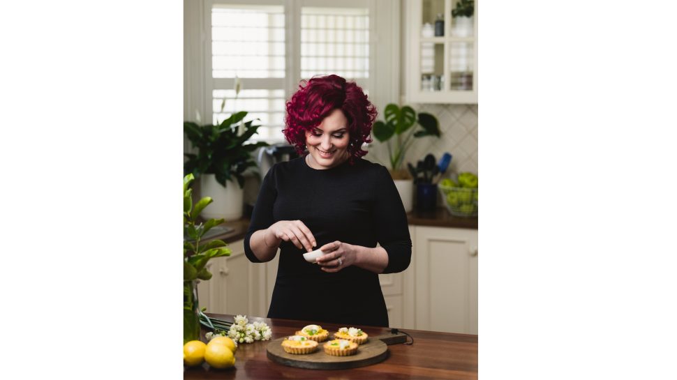 Nikalene Riddle, founder of Skinnymixers, holding a small bowl in front of a kitchen table with desserts on it