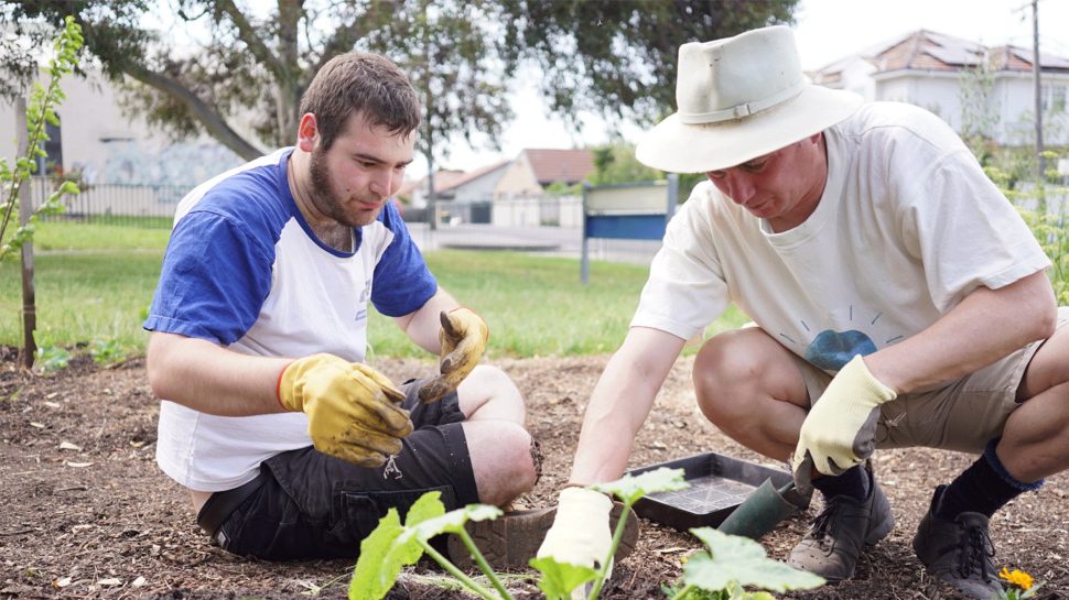 Two med gardening outside with gloves on