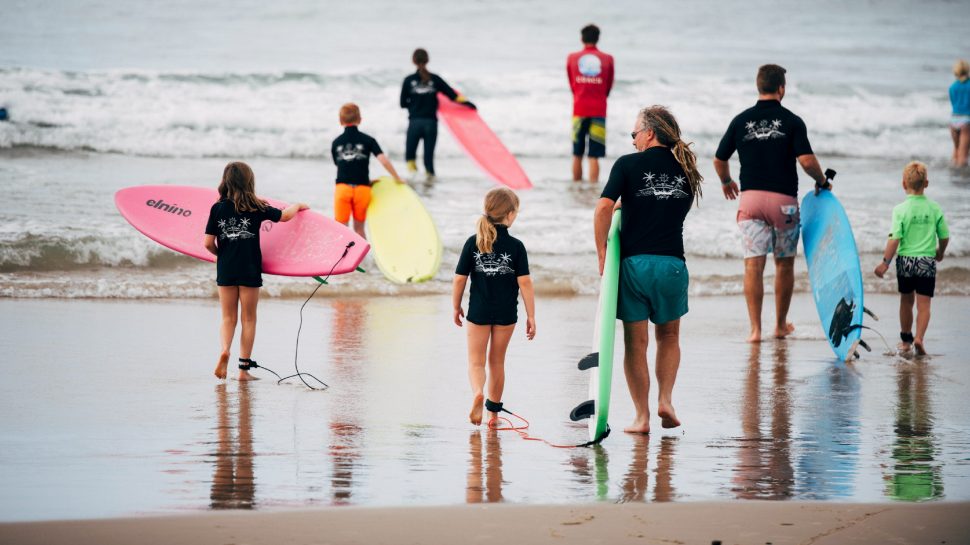Group of adults and kids walking out to catch some waves with their surfboards. 