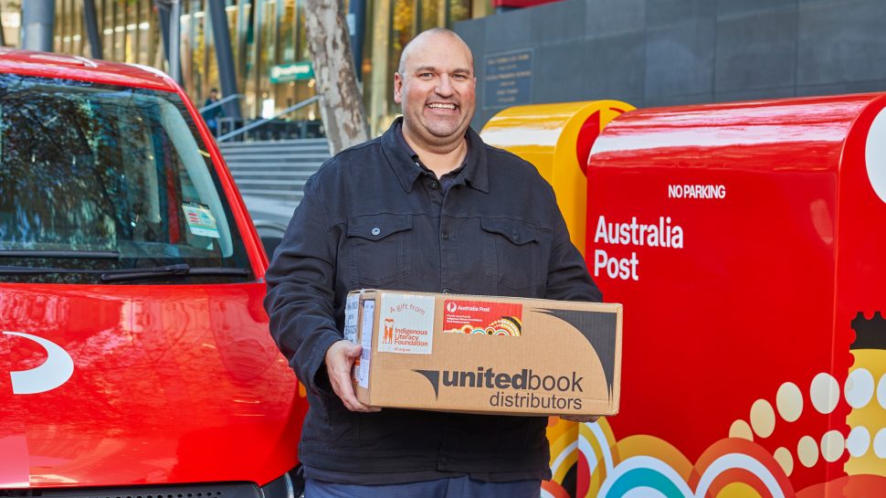 An Australia Post worker holding a box addressed to a Traditional Place Name