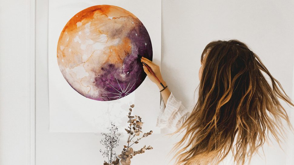 A woman painting a multi-coloured planet on the wall