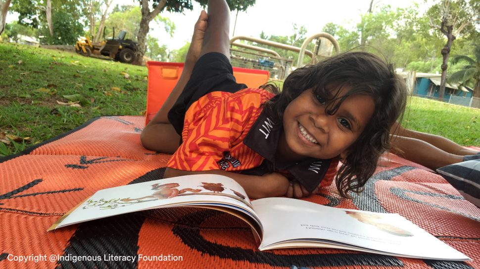 Aboriginal girl smiling while reading a book titled  ‘Possum Magic’.
