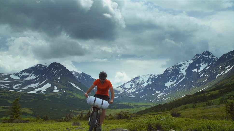 Man on bicycle riding through scenic nature with snowy mountains in the background