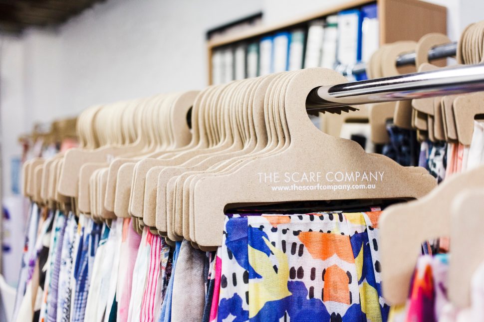 Six white dresses hang from a clothes rack in front of a white brick wall.