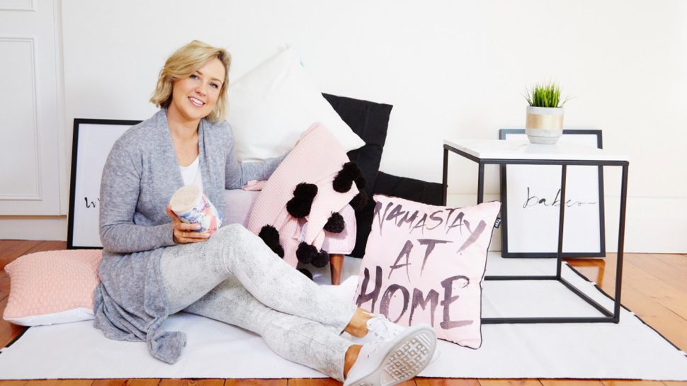 Chelsea Thomas sitting on the floor in her pyjamas, holding a candle, surrounded by pink and white pillows.