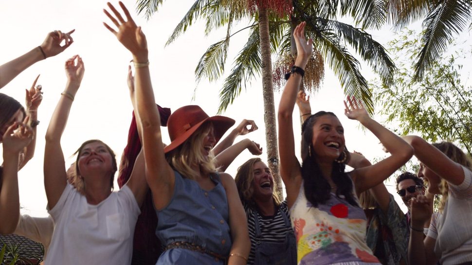 Young folk dancing with hands up under a palm tree