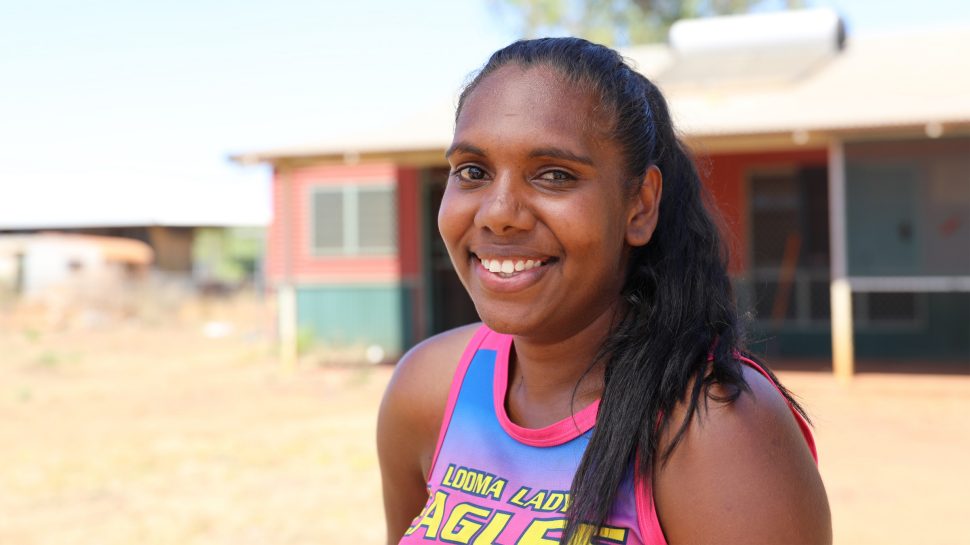A young Indigenous woman wearing a pink singlet with the words Looma Lady Eagles written on it