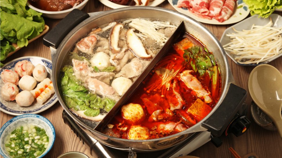 Giant hot pot on table - one side regular style, other side spicy; various meat and vegies in bowls surrounding. 