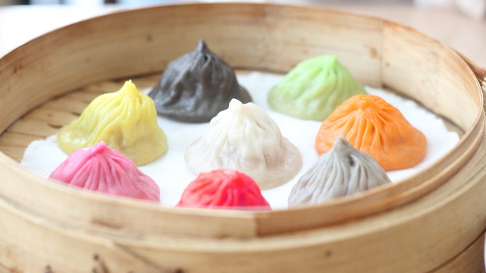 Close-up of 8 colourful xiao long bao in a steamer.
