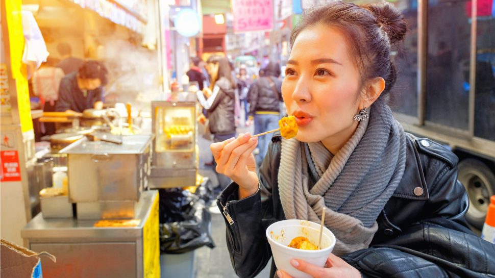 Woman enjoying fried dim sum from a street market stall.