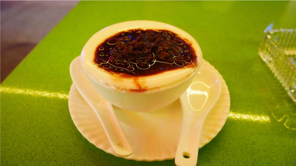 Bowl of milk pudding on a table with red bean topping.