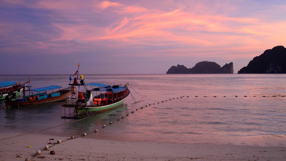 Ko Phi Phi Don beach (largest of the Phi Phi Isalnds in the Krabi province, Thailand) at sunset, with two boats docked in shallow waters in the foreground. 