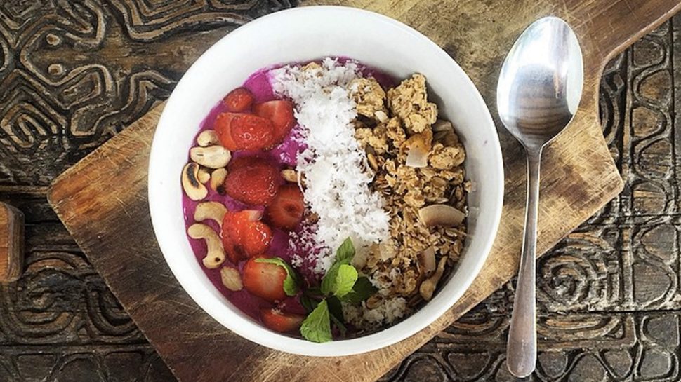 A birds-eye-view of Brooke sitting at a table at the Betelnut Café. On the table in front of her is the “Naga Bowl”—a dragon-fruit breakfast bowl topped with granola, fruits and superfoods. 