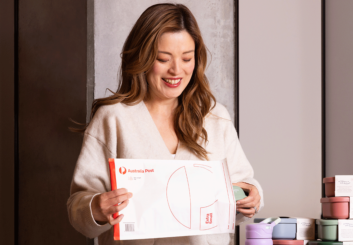 A woman is packing orders intoc Australia Post branded flat rate pakaging boxes